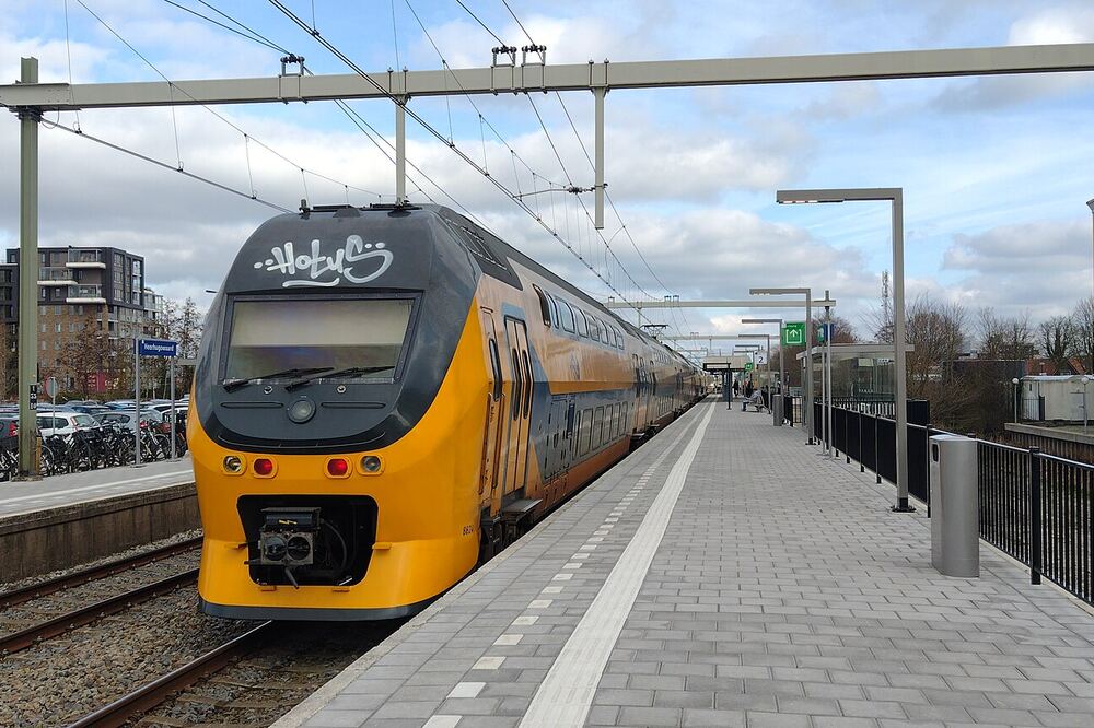 Gele NS-intercity langs het perron van station Heerhugowaard, met nieuwbouw van het Stationskwartier op de achtergrond