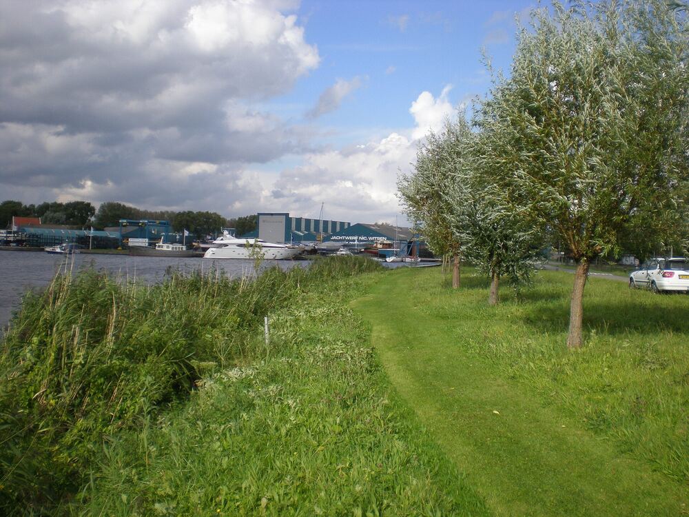 Groene oever met bomenrij en bootjes aan het begin van het Kanaal Omval-Kolhorn bij Heerhugowaard
